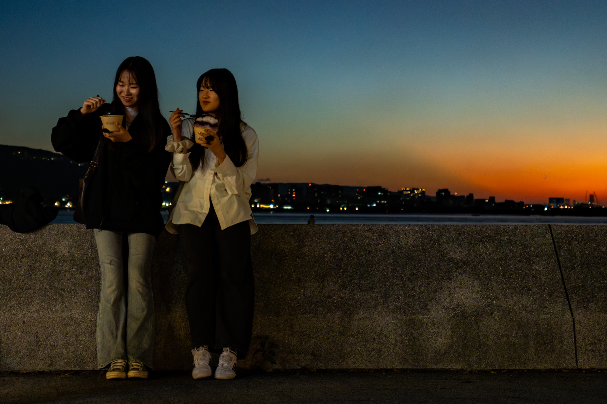 Two people eating ice cream by the waterfront at dusk